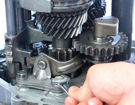 Close-up of exposed metal gears and a hand using a wrench to adjust a machine assembly