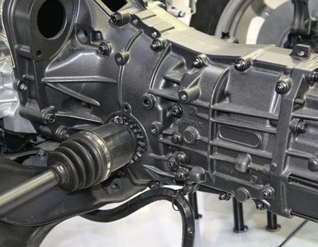 Close-up of a car transmission assembly with a driveshaft and bolts in a workshop setting