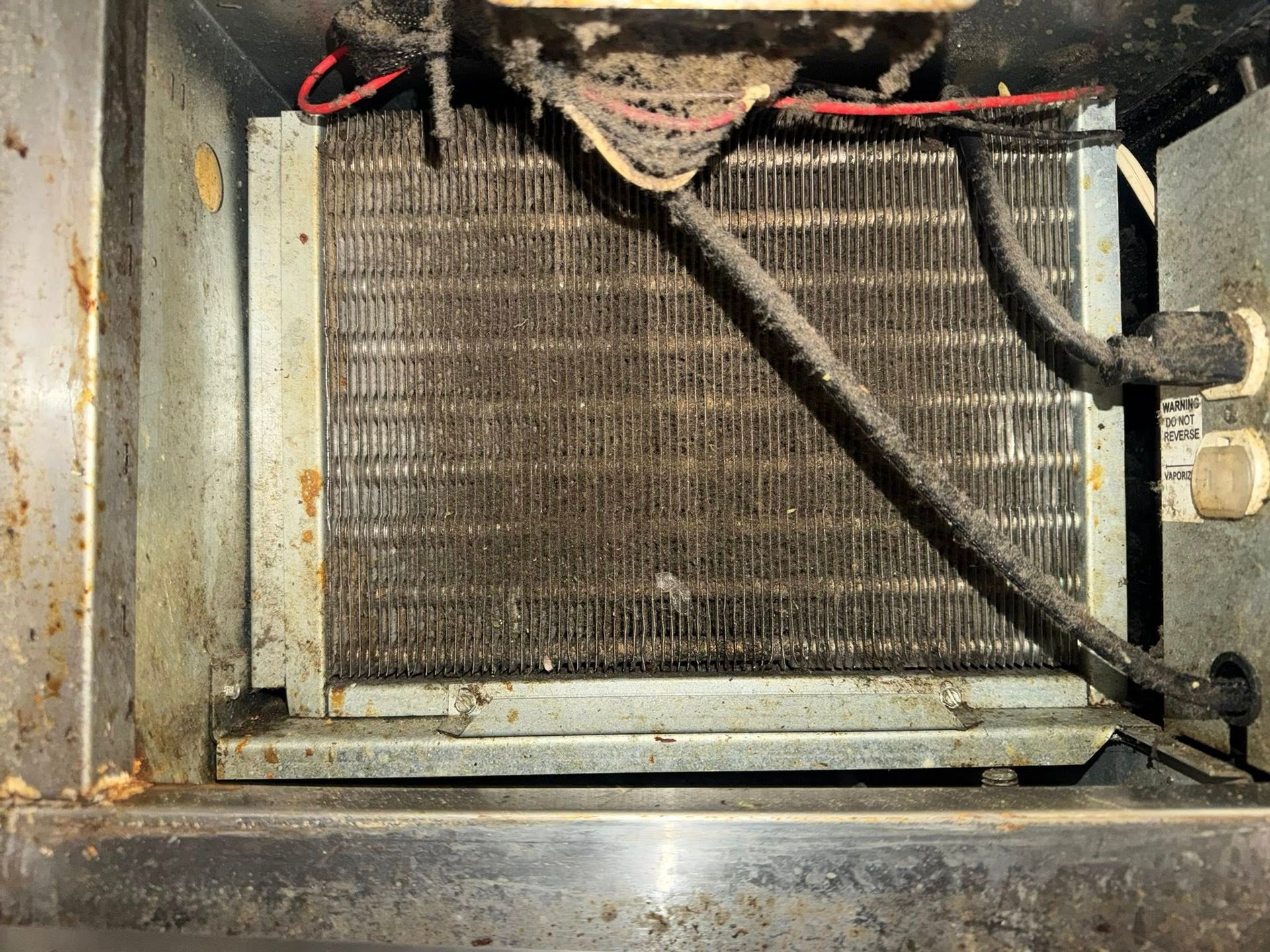 Dirty HVAC condenser coil with black hoses and red wiring inside a metal unit