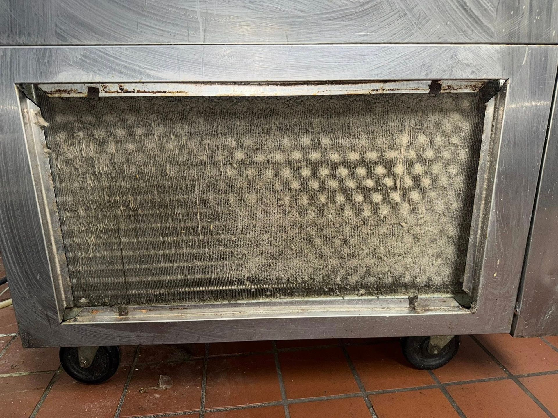 Metal front panel with a recessed mesh grille and two wheels at the bottom.