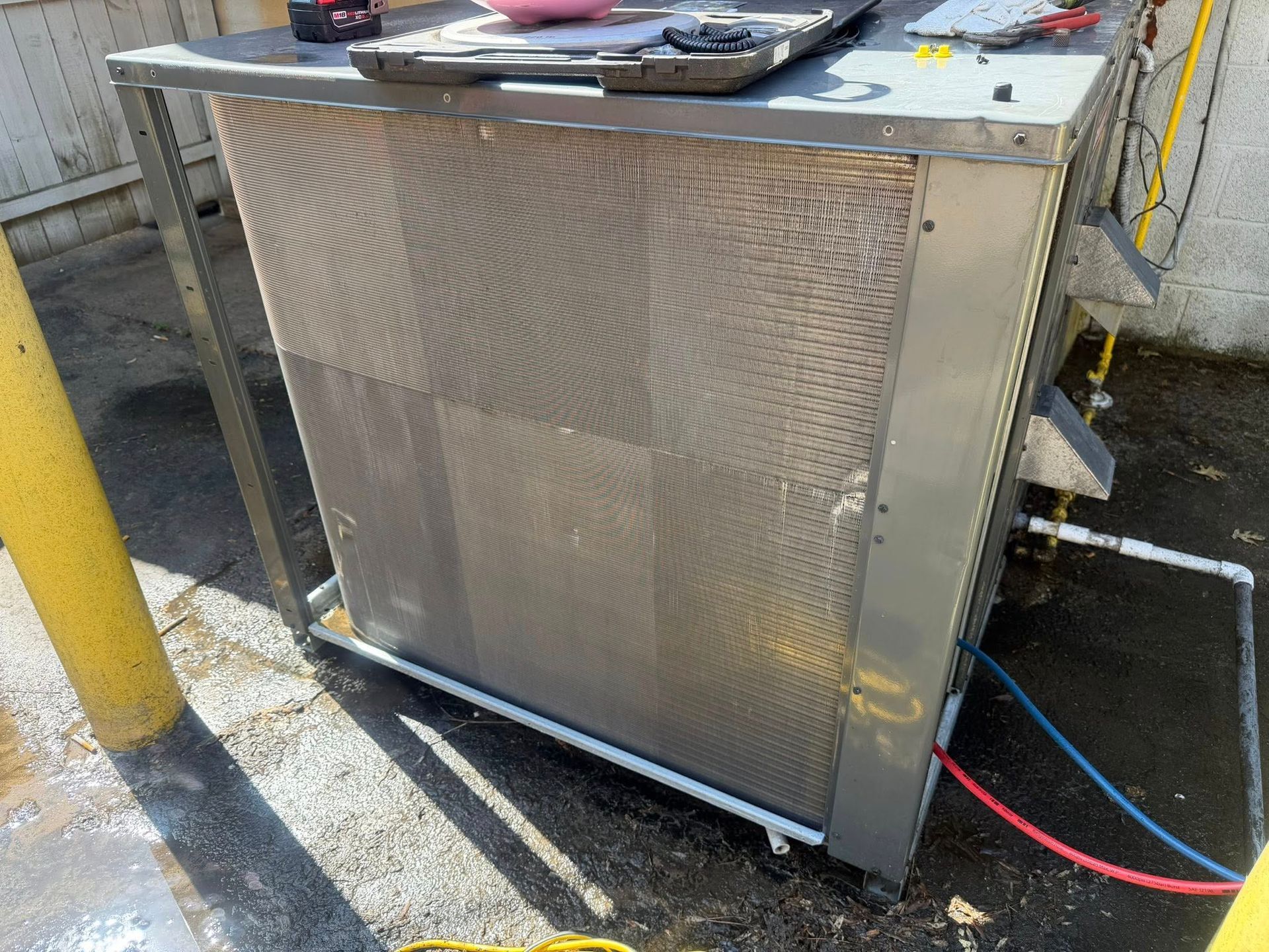 Outdoor metal equipment cabinet with perforated front panel, pipes, and red and blue cables attached