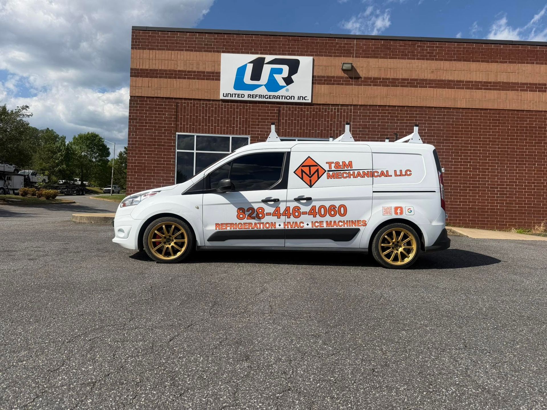 Branded white van with gold wheels parked outside a brick building with a UR sign