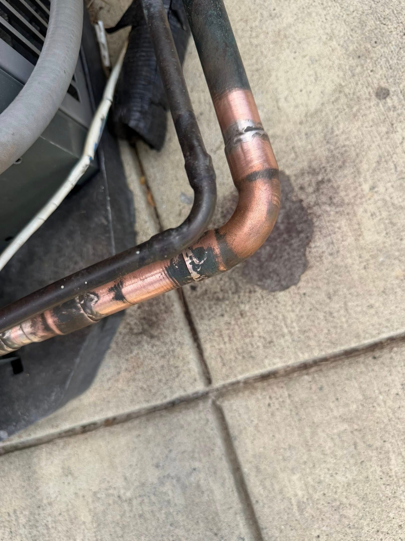 Copper pipe elbow joint with dark stains, running along a concrete floor.
