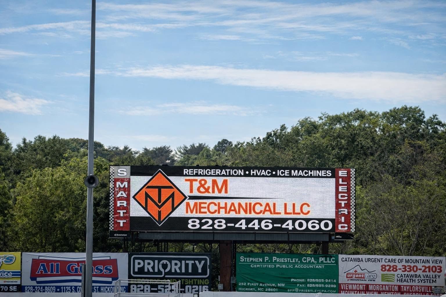 Billboard for T&M Mechanical LLC with orange logo, phone number, and advertisements along a roadside