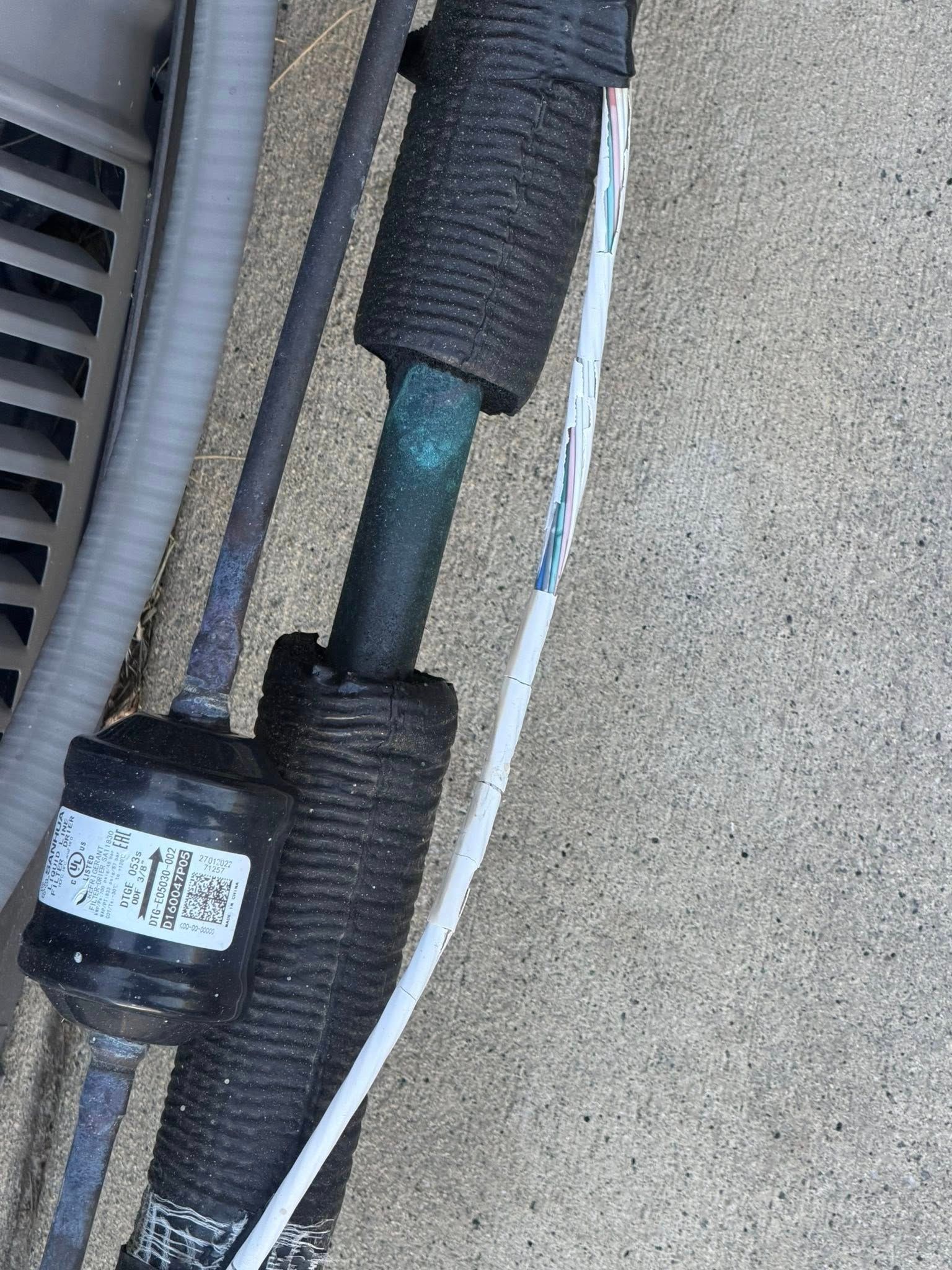 Close-up of insulated pipes and cables against a beige wall outdoors.