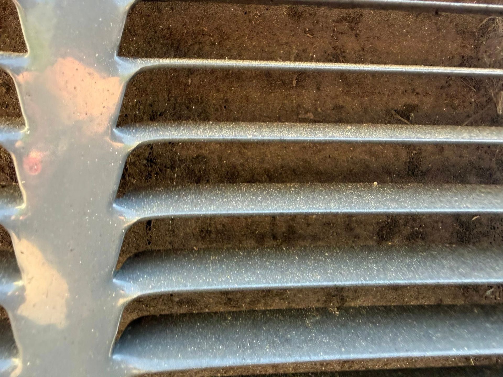 Close-up of a silver metal vent grille with horizontal slats and dust buildup
