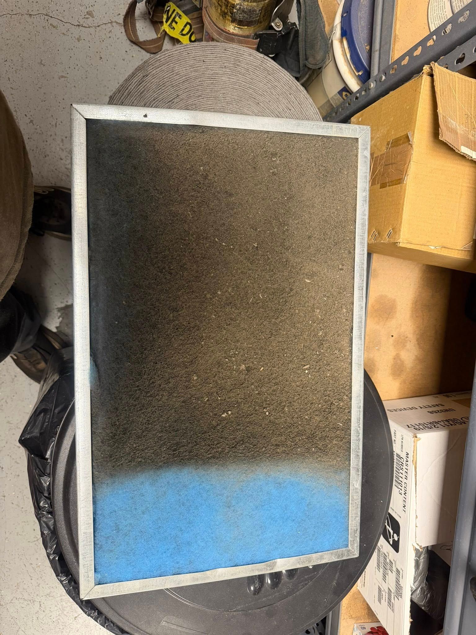 Rectangular black-and-white framed object with a blue bottom section, leaning in a cluttered storage area