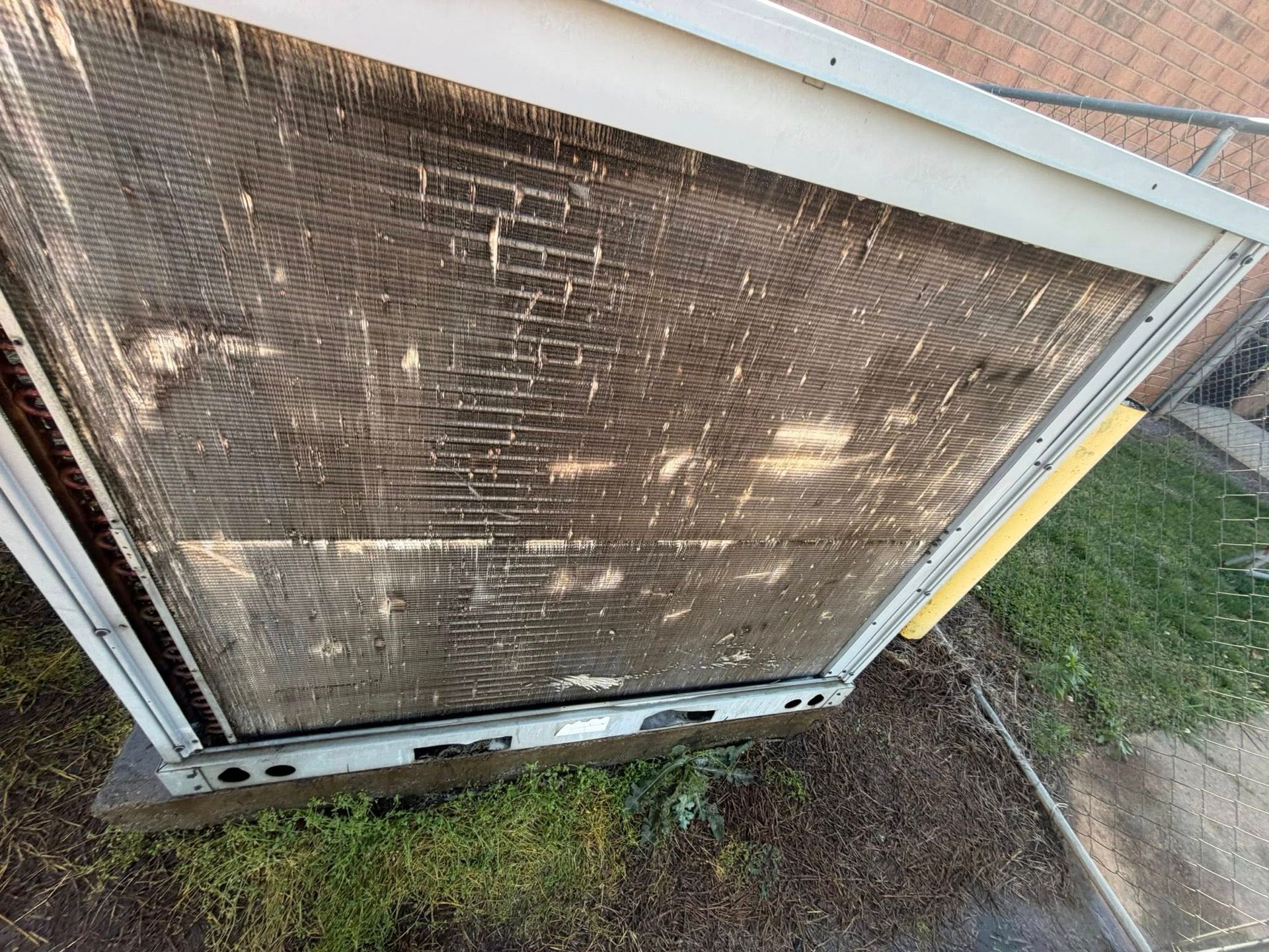 Dirty window AC unit with a rusted metal grille outside a house