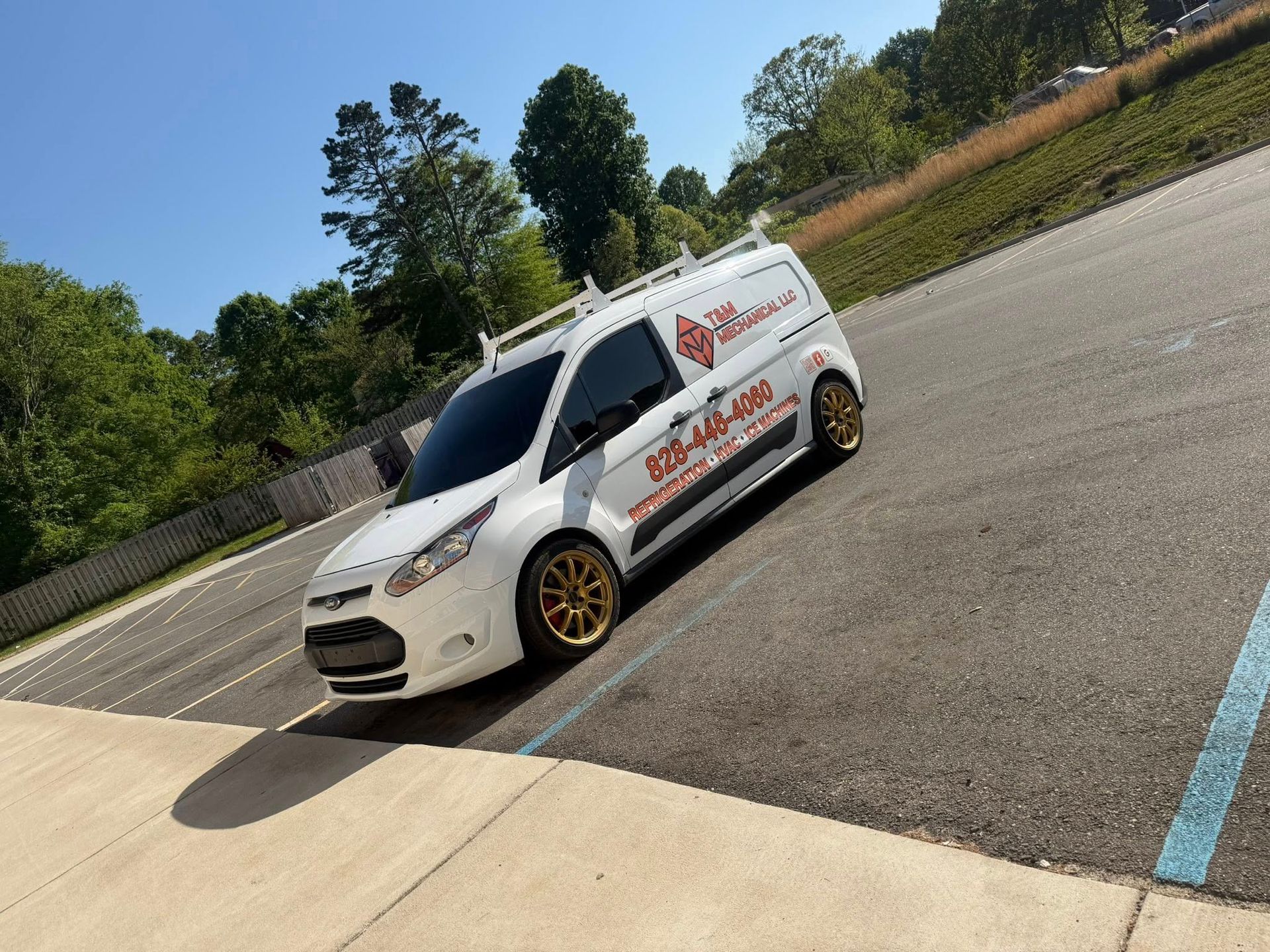 White delivery van with orange lettering parked on a slanted road in a sunny outdoor lot