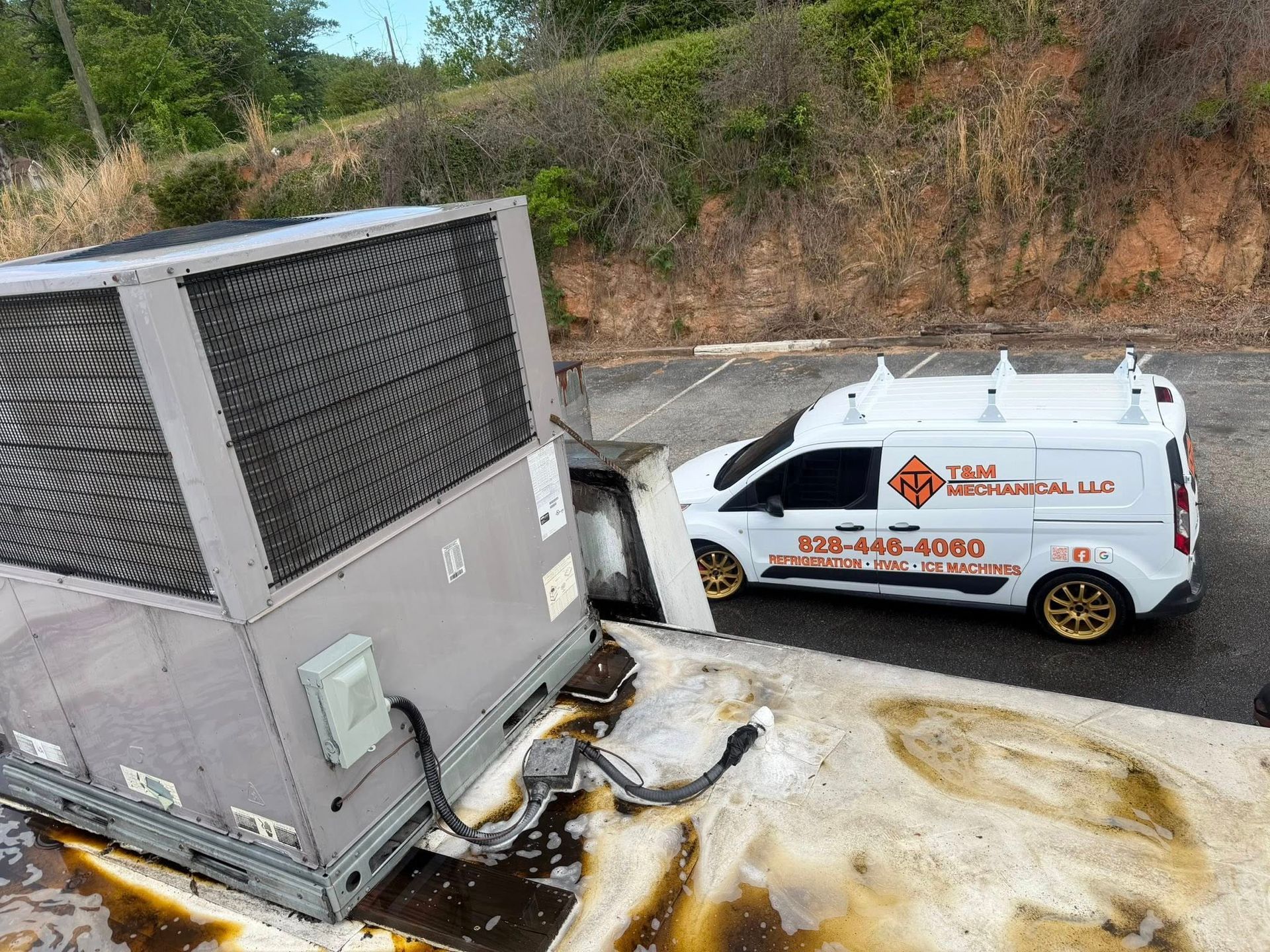 HVAC service van parked beside a large rooftop unit with spilled foam or coolant on the ground