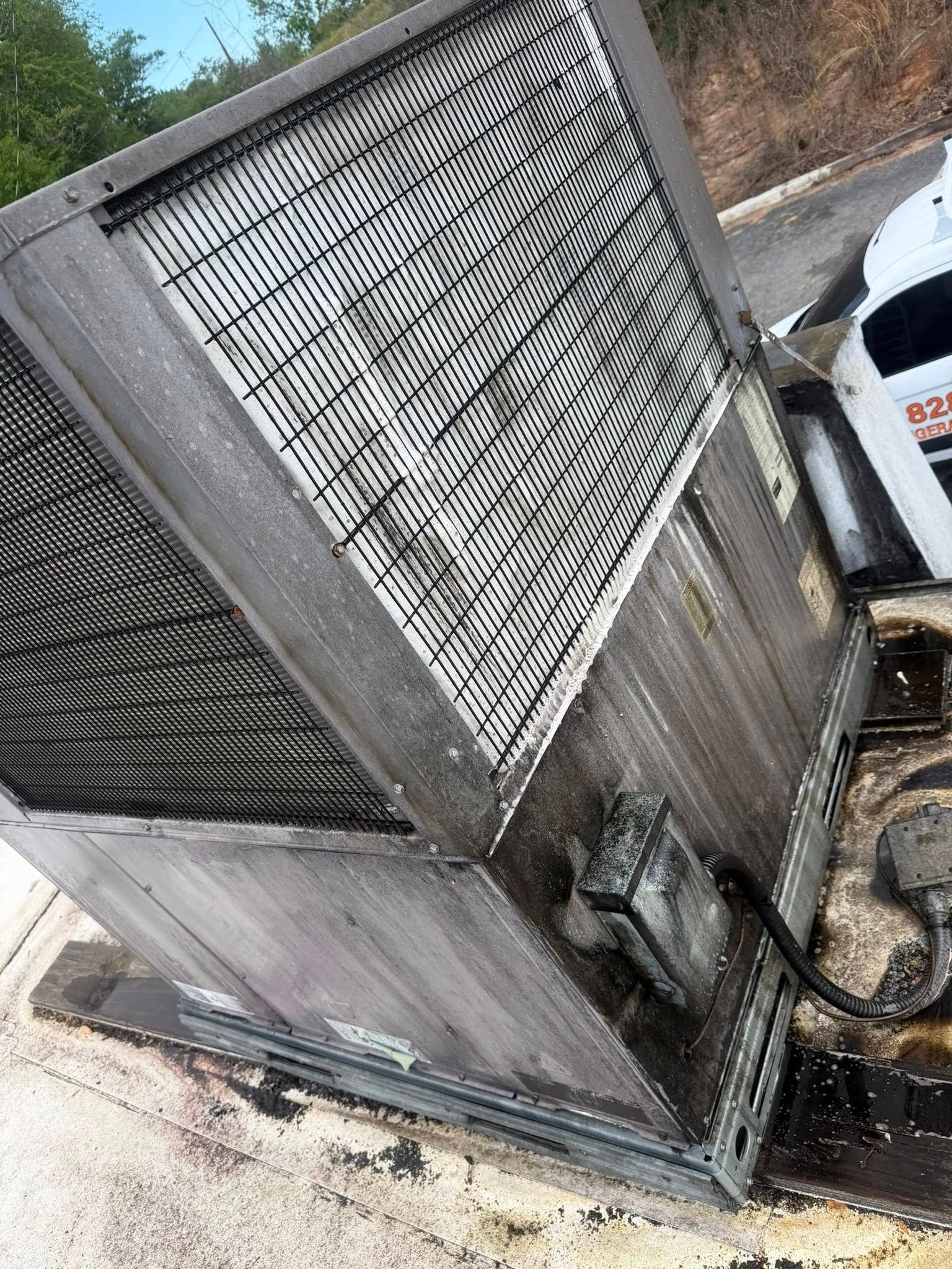 Large metal cooling unit leaning on its side beside a parked white vehicle outdoors