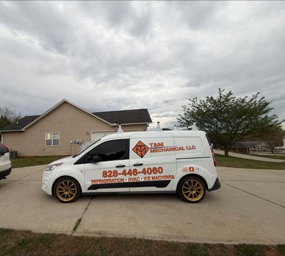 White service van with orange lettering and gold rims parked in a driveway beside a house under cloudy skies
