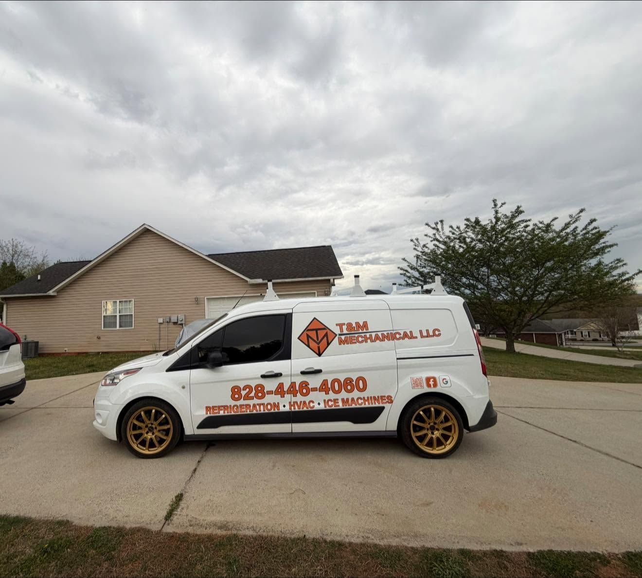 White service van with orange lettering parked in a driveway beside a house under a cloudy sky.
