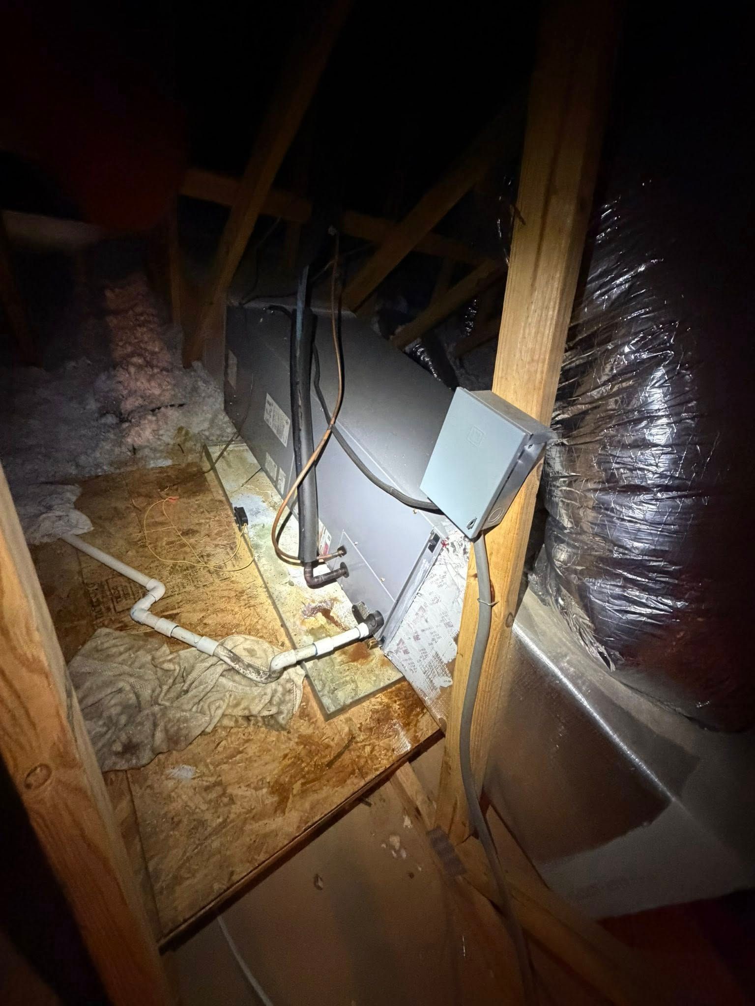 Attic with exposed insulation, ducts, and electrical wiring under wooden rafters