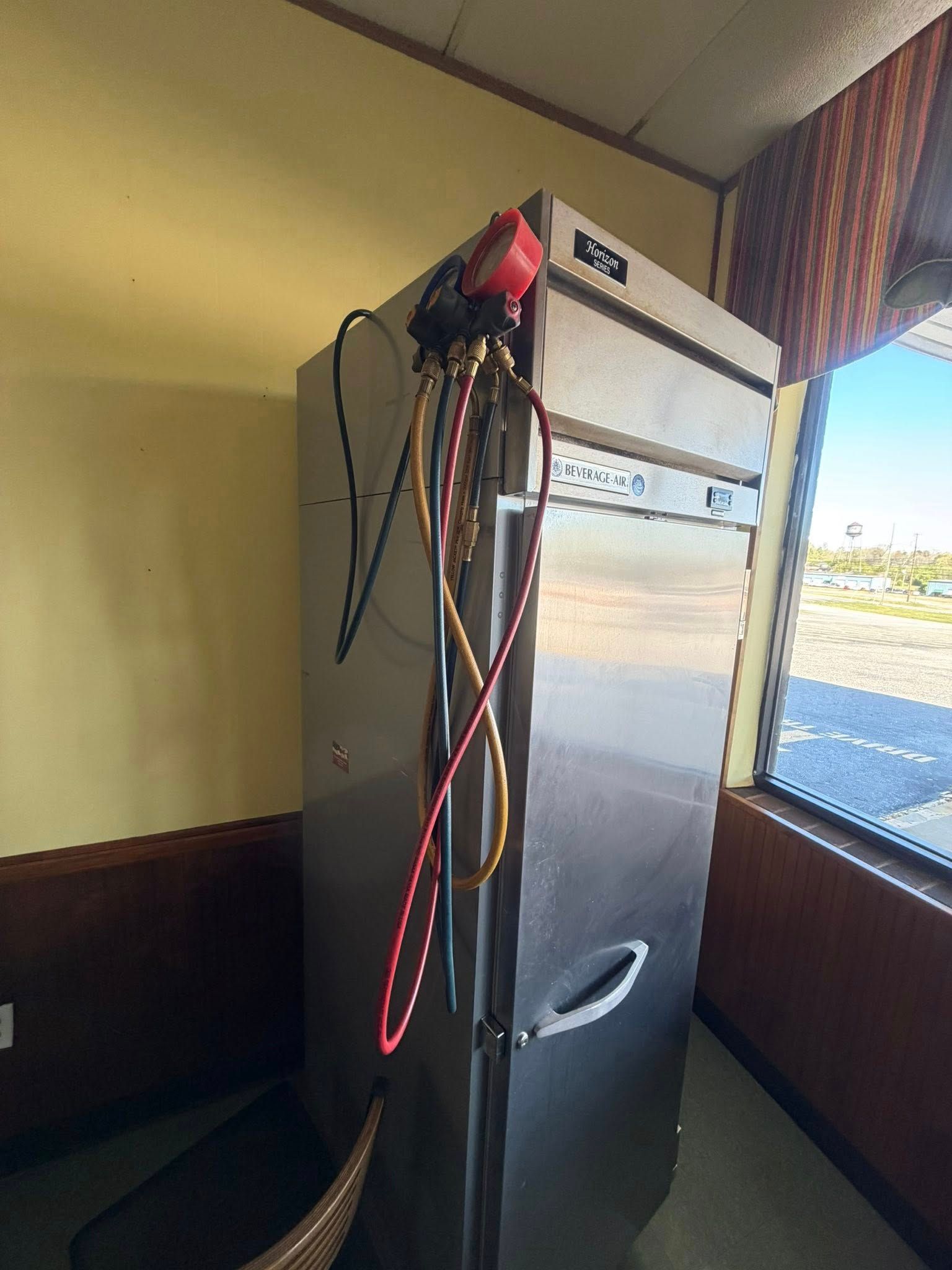 Tall metal cabinet by a window with several cables hanging from the top.