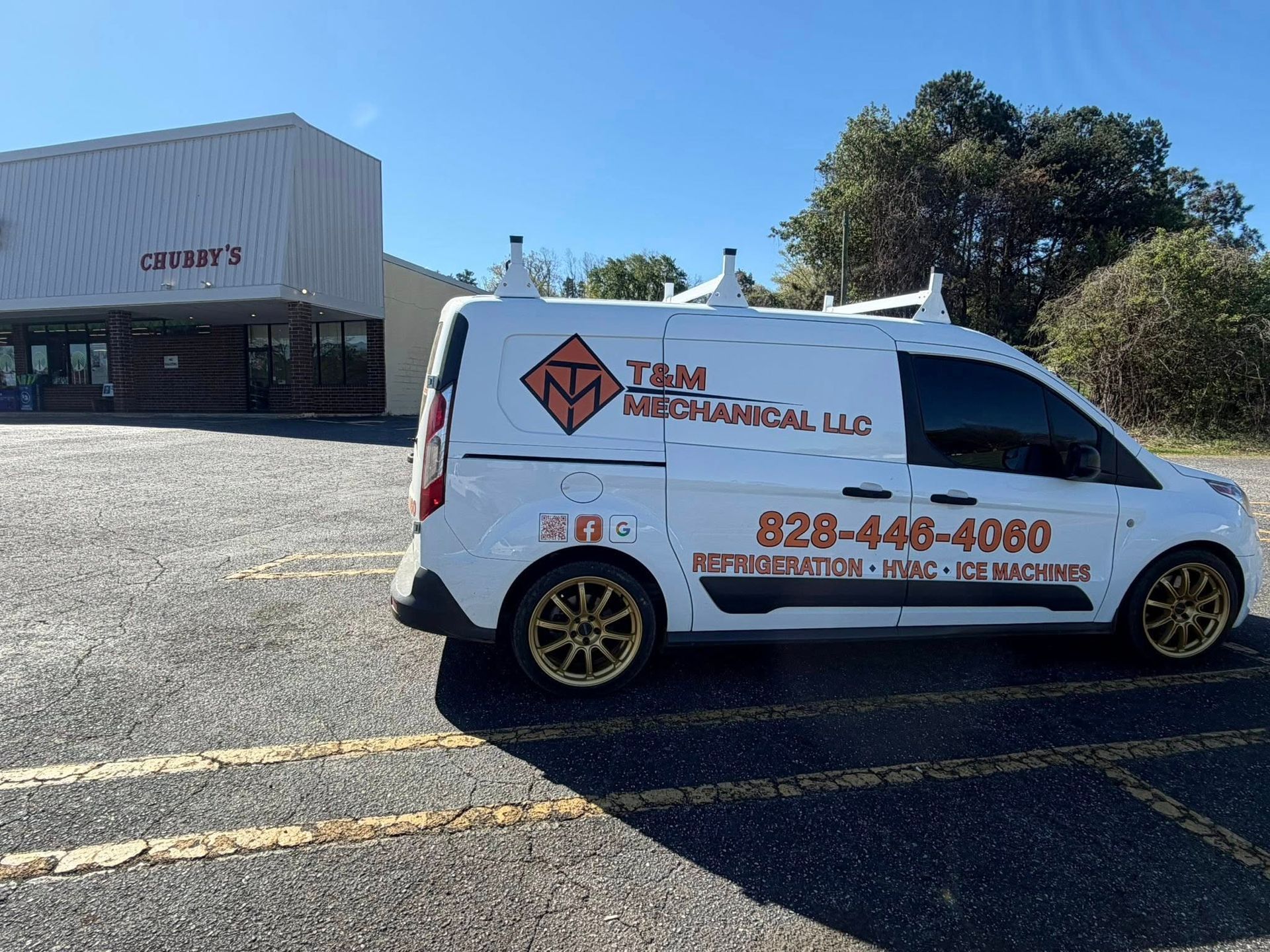 White plumbing service van parked in a lot beside a building, with company logo and phone number on the side