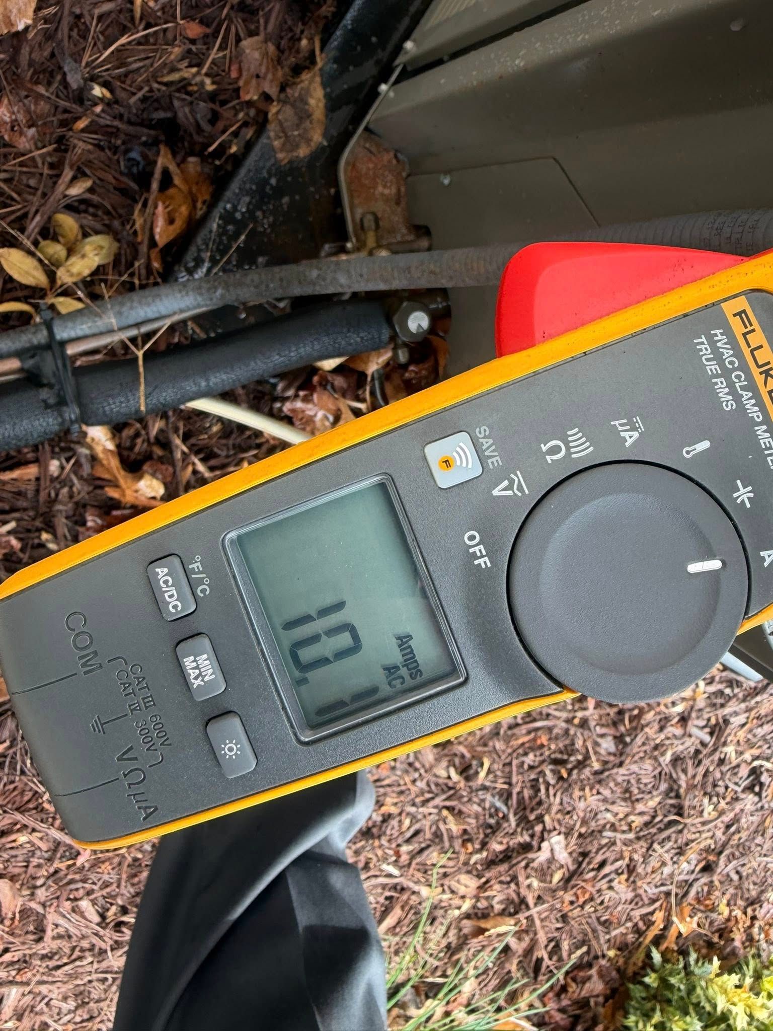 Digital multimeter on mulch, showing a reading while connected to black wires.