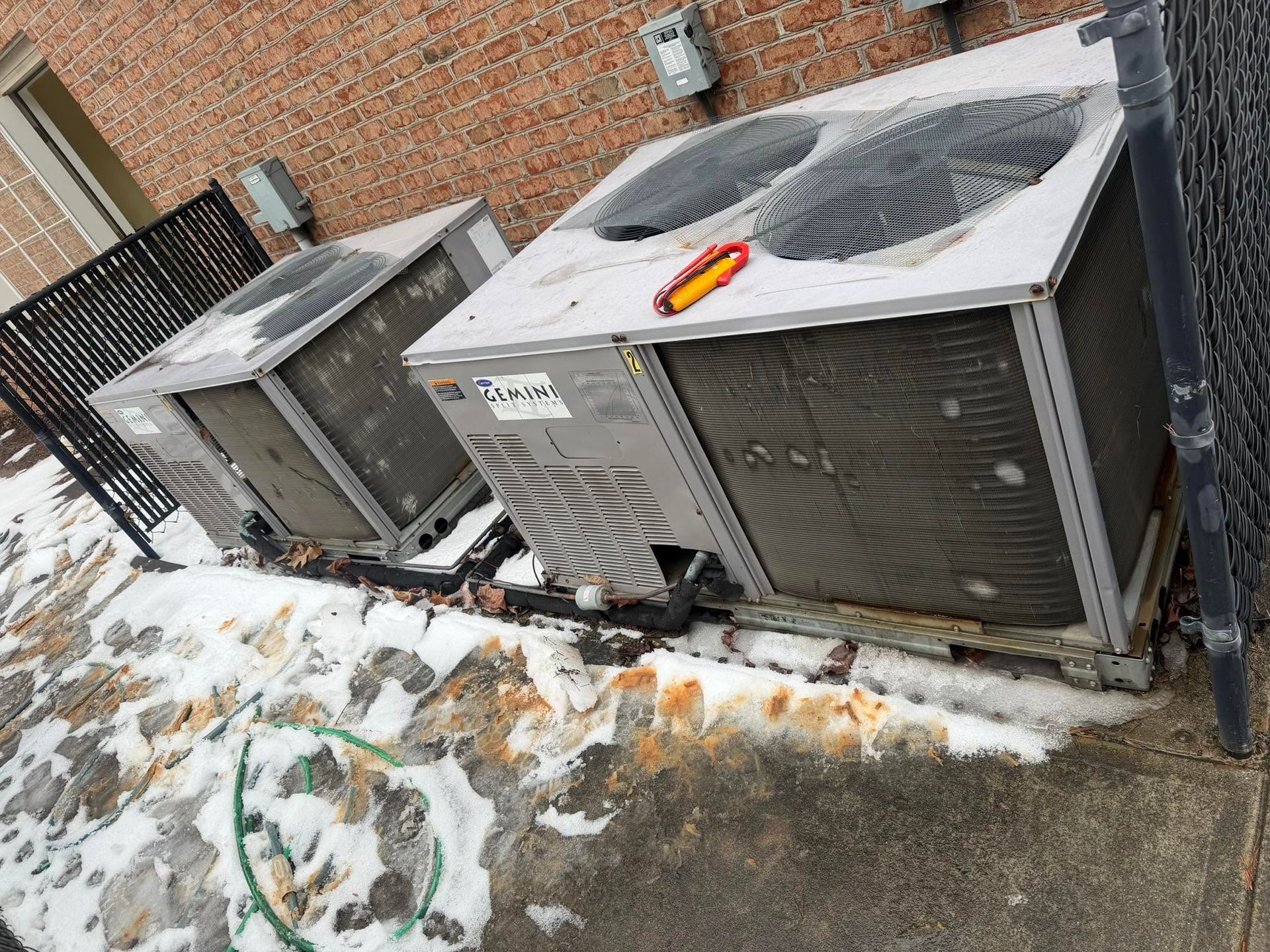 Outdoor HVAC units beside a brick building, with snow and ice on the ground.