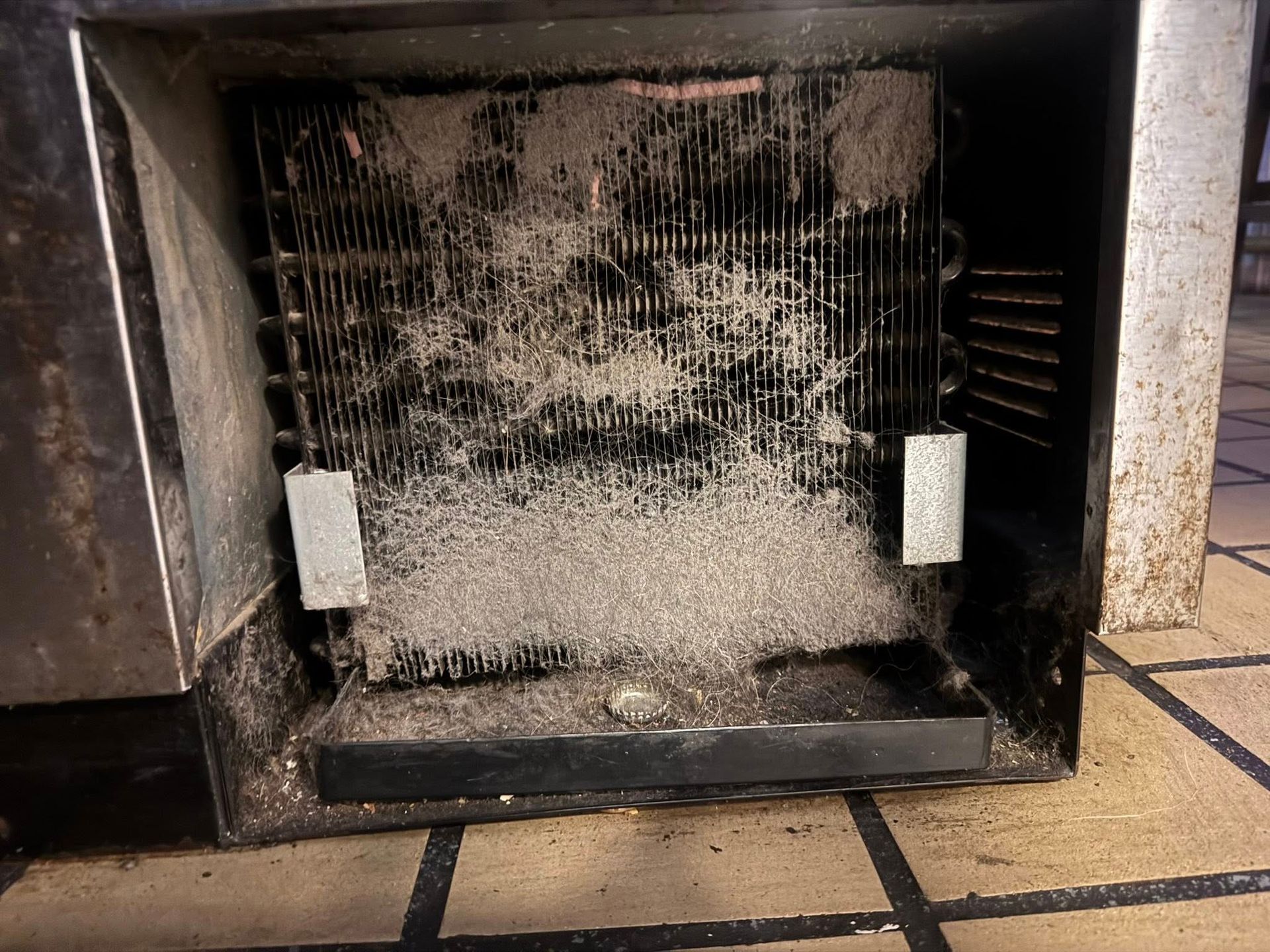 Dust-covered air vent or HVAC filter with two white clips, set in a dirty floor opening