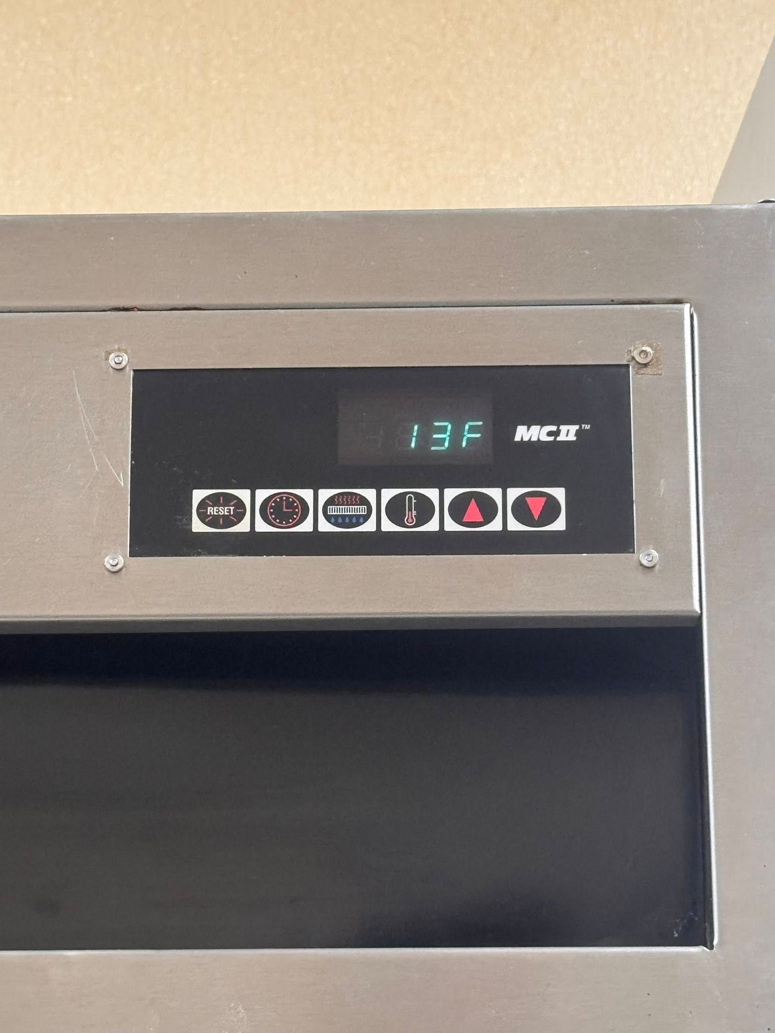 Wall-mounted control panel with digital display and buttons above a black opening.