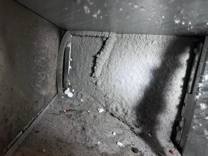 Dust-covered interior of a metal duct or vent with grime buildup and debris.