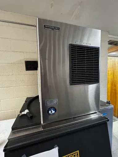 Stainless steel industrial machine on a black base in a utility room, with a vented front panel.
