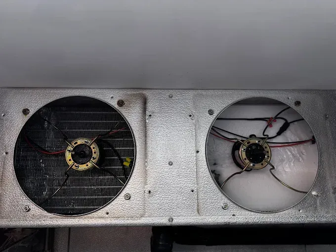 Two large industrial fans in a metal panel, one dark and one white with exposed wires.