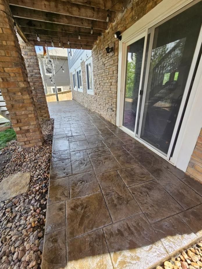 Brown stamped concrete patio under a covered porch with a sliding glass door and brick and stone accents.