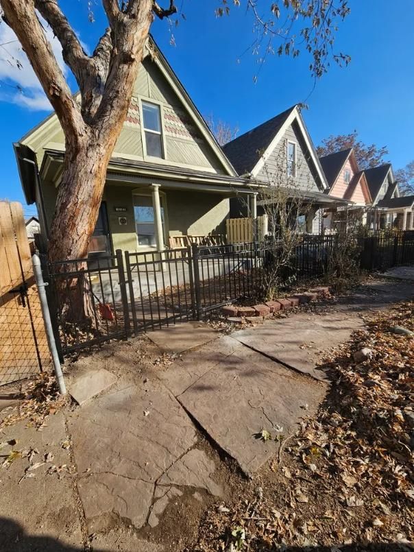 Houses on a street, the first with a black fence and a porch. 