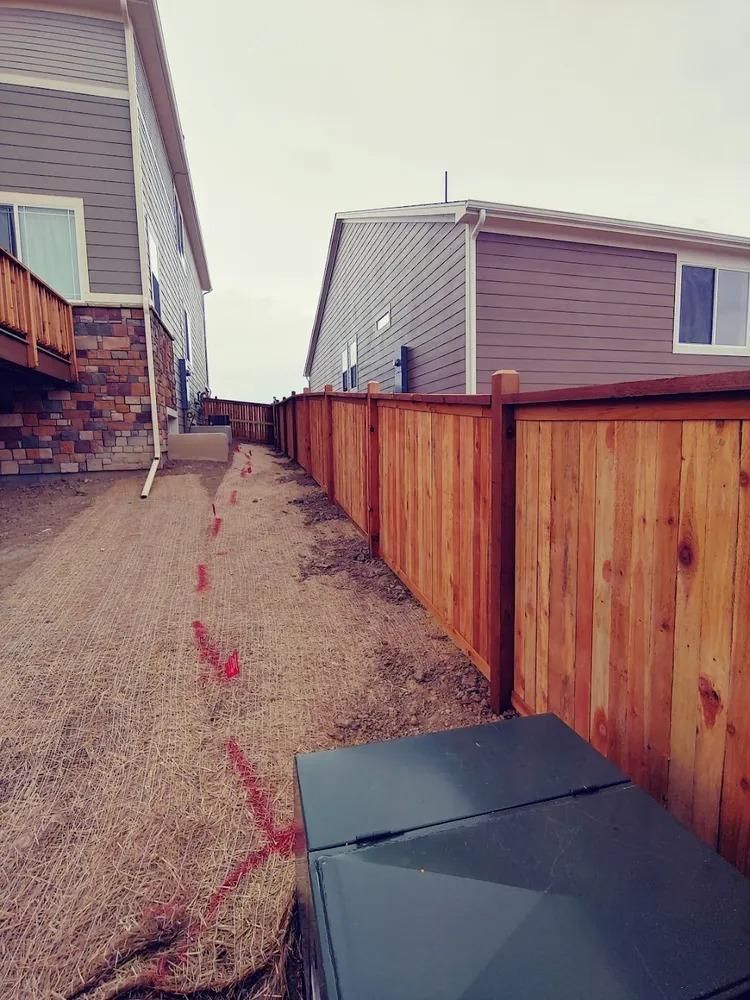 Narrow gravel path between two houses, new wooden fence on one side.