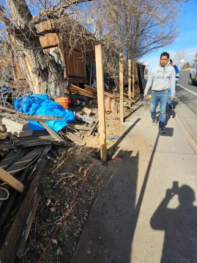 Sidewalk scene with a man walking past a partially demolished wooden structure and a roadside.