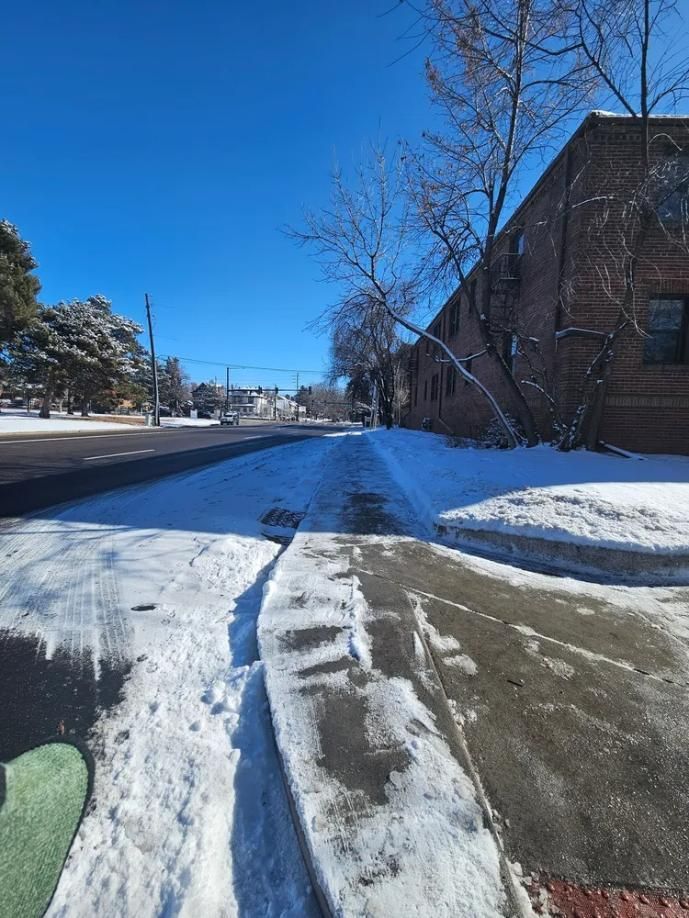 Snowy street scene, brick building on right, sidewalk partially clear, blue sky.