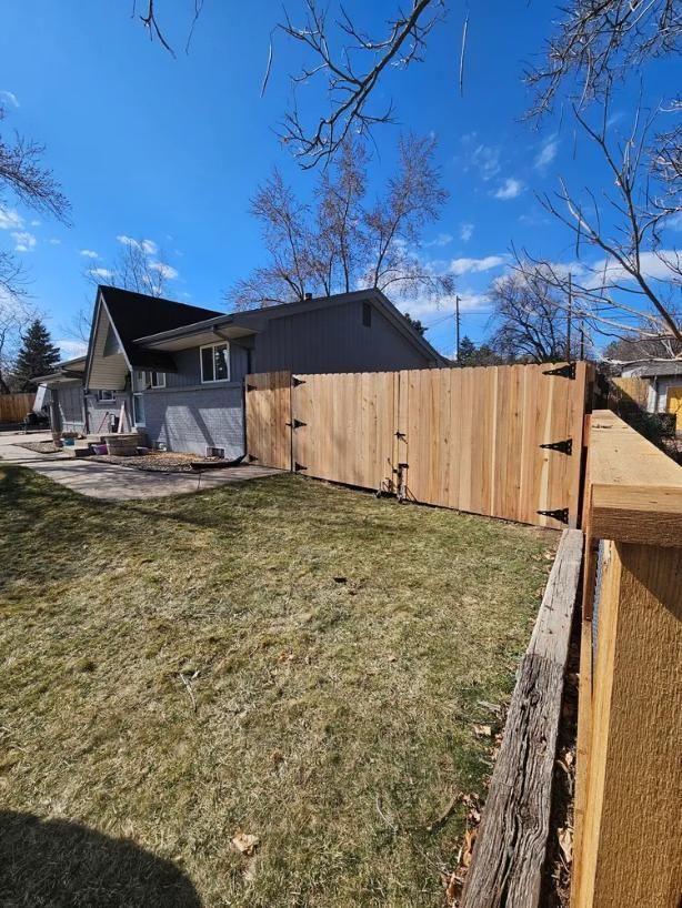 Wooden fence in a backyard, beside a house with gray siding. 
