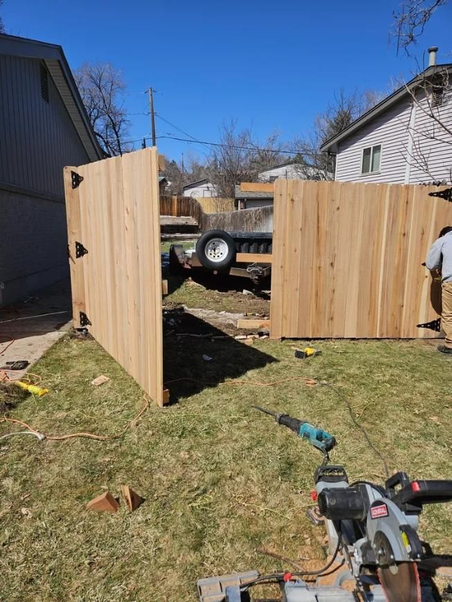 Wooden fence panels being built outdoors; person working, tools visible, blue sky.