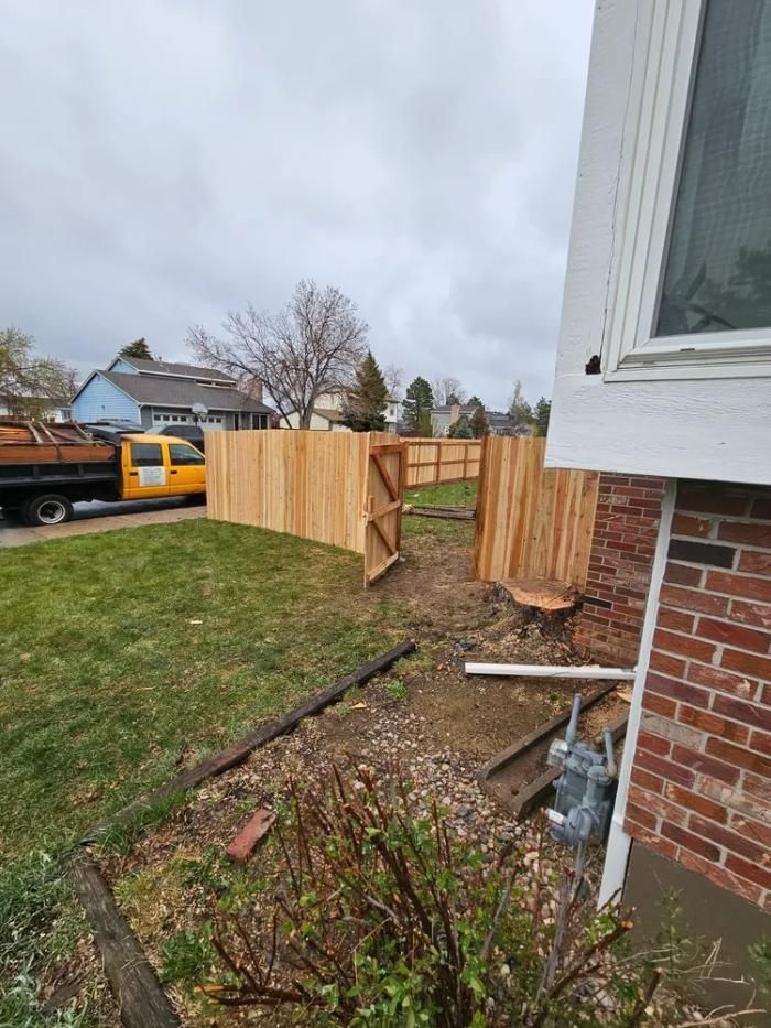 Wooden fence being built in front yard next to a brick building. 