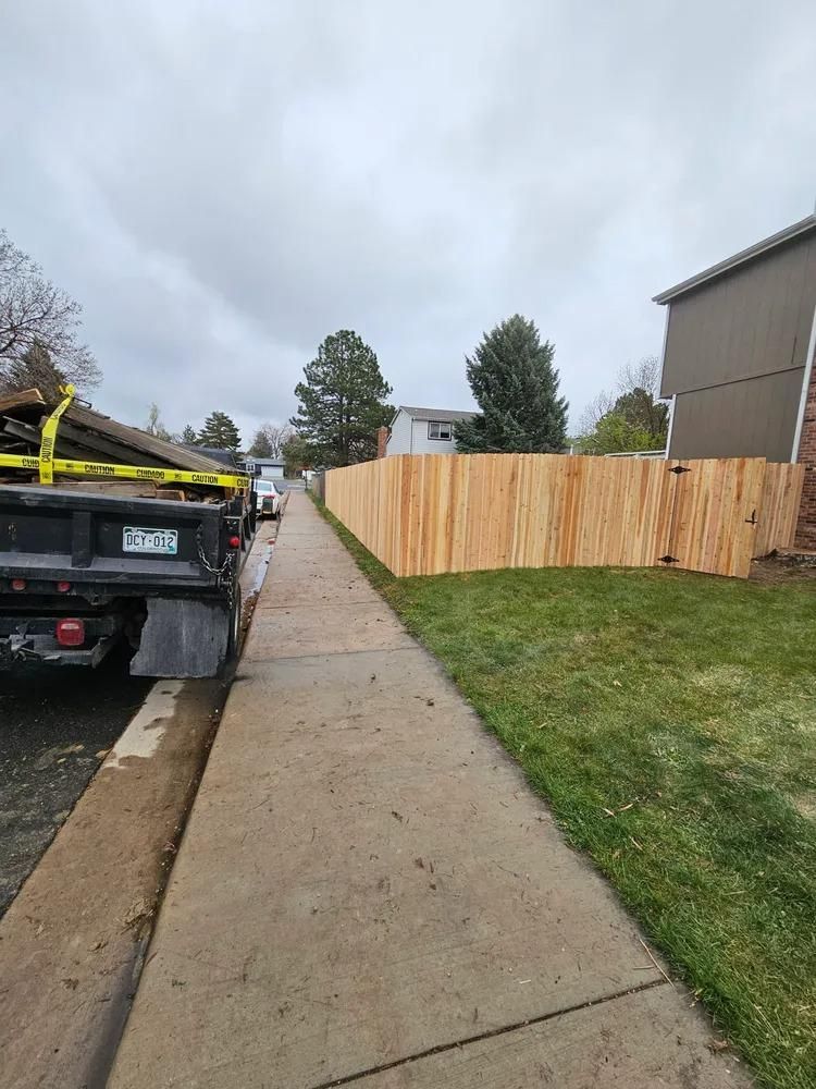 A truck beside a sidewalk next to a newly built wooden fence on a grassy lawn.