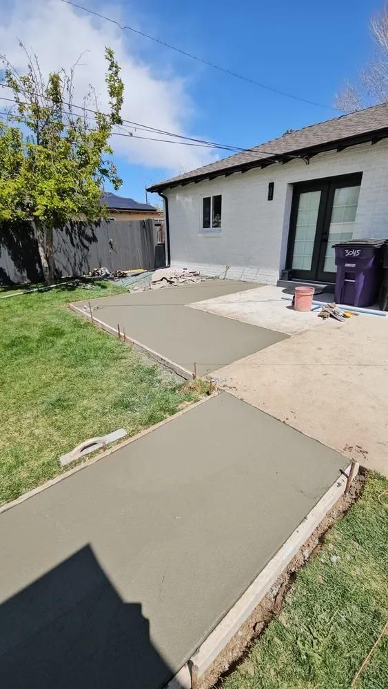 Newly poured concrete walkway in a backyard, leading to a house. 