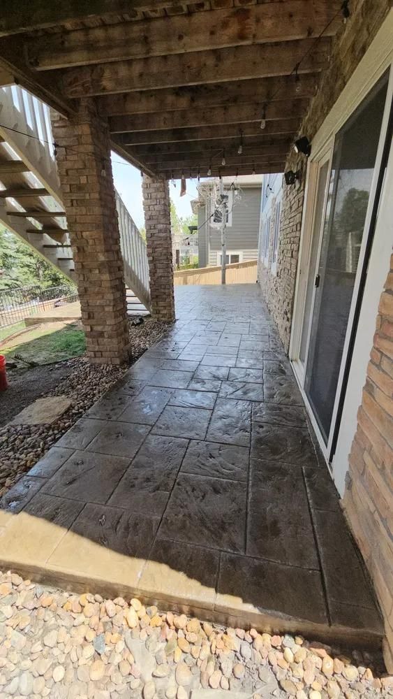 Stone stamped concrete walkway under a deck with brick columns.  