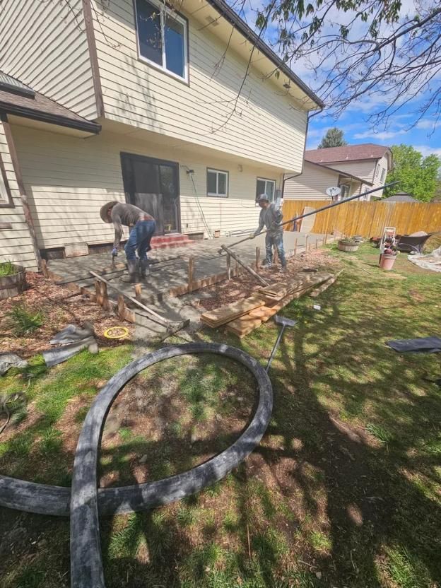 Two workers removing a patio near a house with a hose in the foreground.