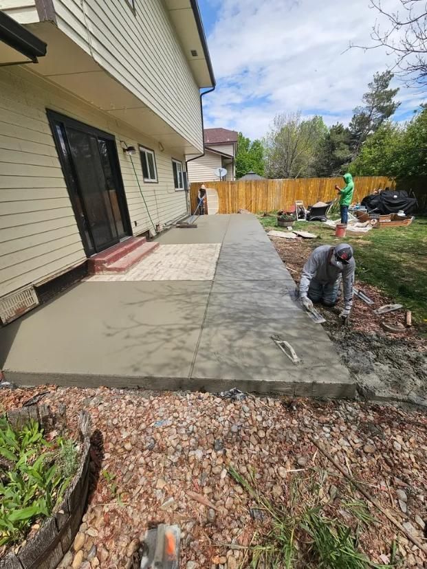 Construction workers pouring concrete for a patio. Building next to a yard with fence. 