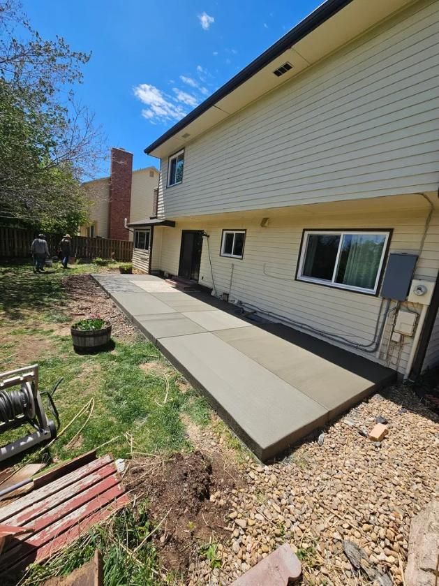 A new concrete patio extends from the back of a light-colored house. 