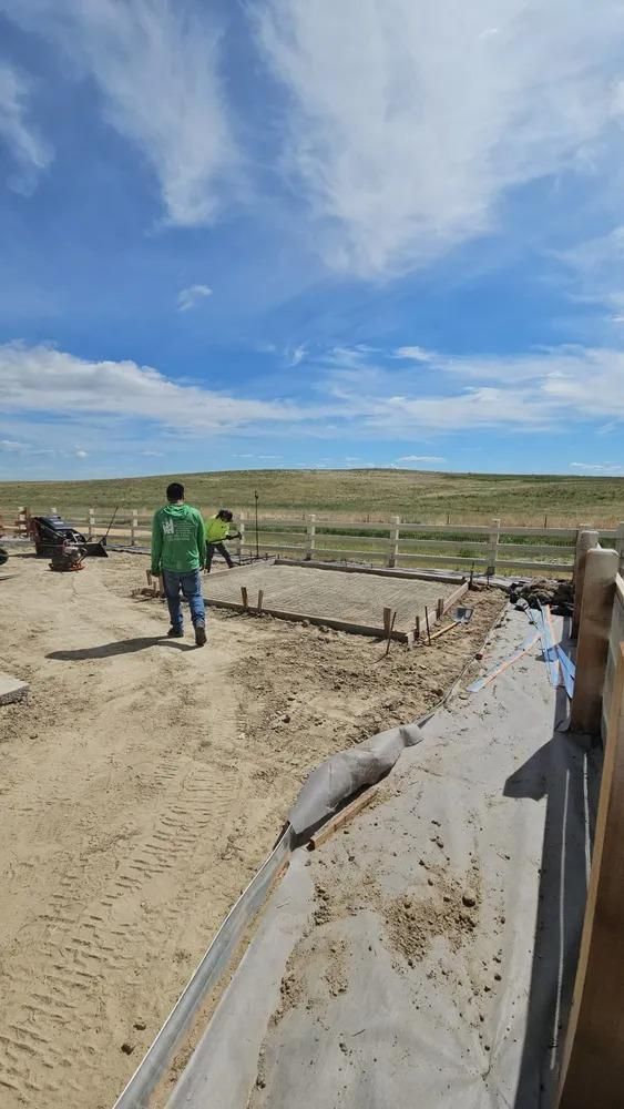 Construction site with workers, foundation framework, clear sky, outdoor setting.