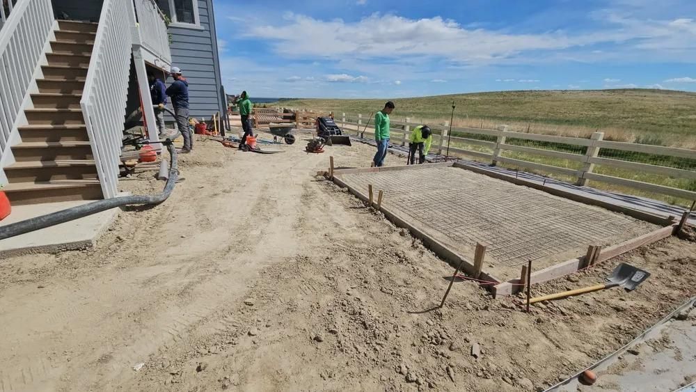 Construction workers pouring concrete for a patio next to a house, bright sunny day.