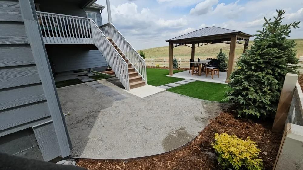 Backyard with a deck, stairs, patio, gazebo, green grass, and small plants.