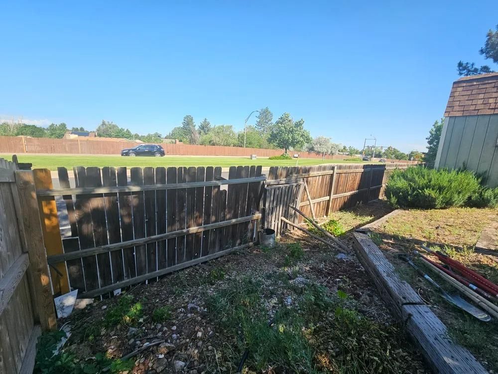 Wooden fence, gate, and debris in a yard on a sunny day.