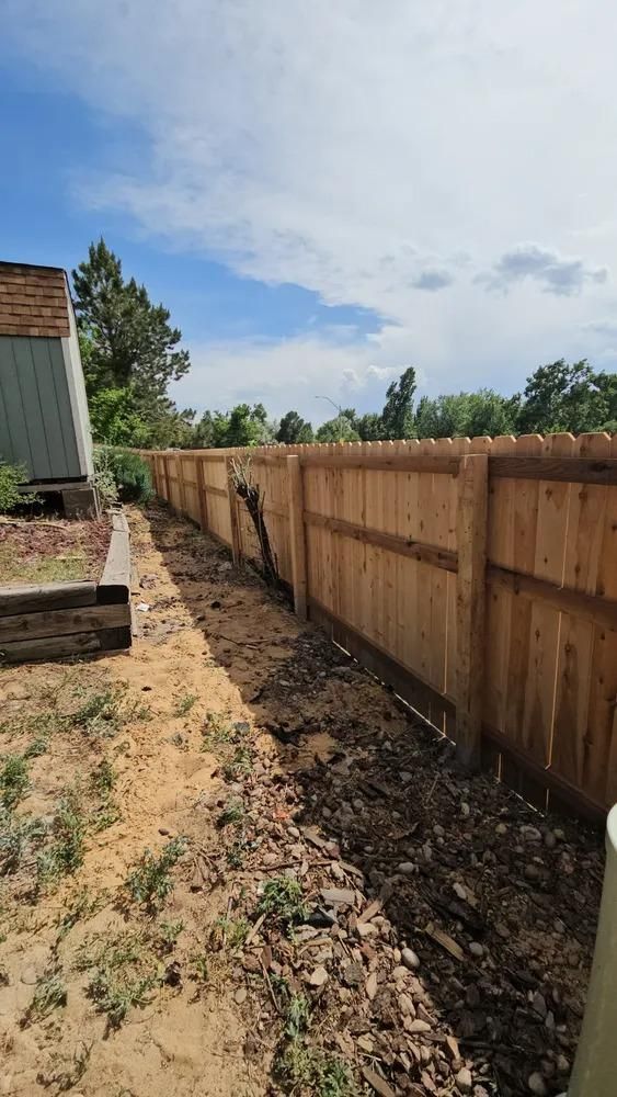 New wooden fence along a yard, with disturbed earth and sky visible.