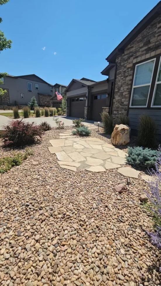 Stone pathway leads to house with gravel landscaping, blue sky.
