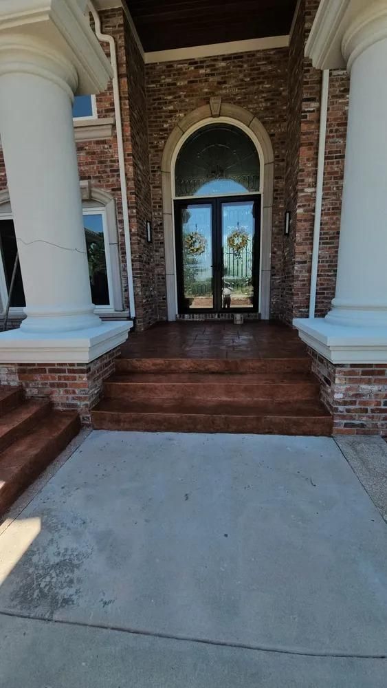 Front entrance of a house with columns, brickwork, and double doors. 