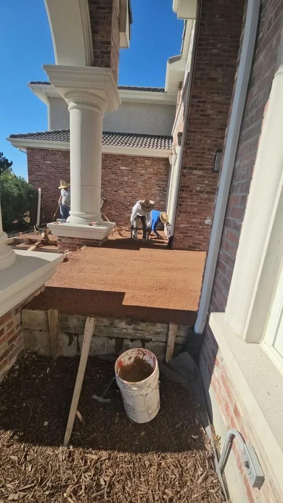 Construction site; workers building a brick patio next to a house with white columns.
