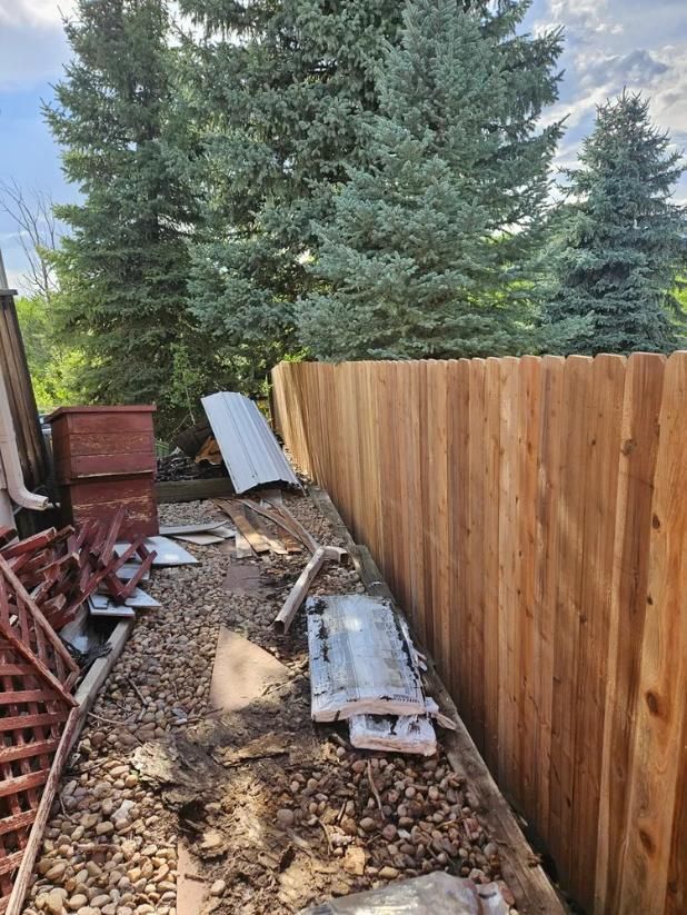 A new wooden fence next to debris and trees against a blue sky.